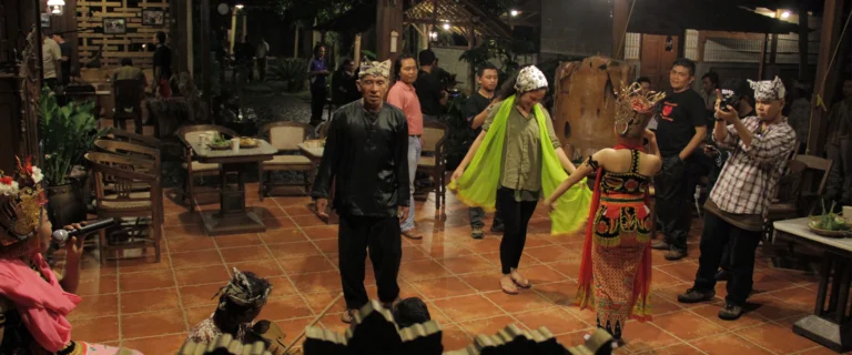 Film crew recording a traditional dancer in a green cloth inside a cafe