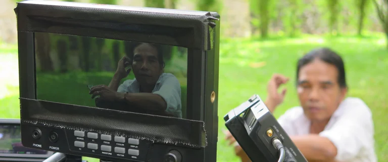 Camera monitor in the foreground with a man smiling beside it during filming