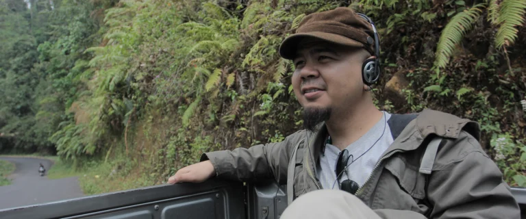 Man with a cap and headphones riding in a truck bed on a forested mountain road